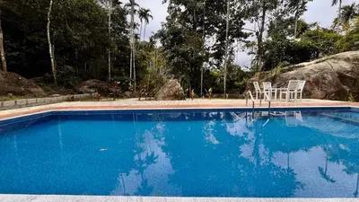 a swimming pool with two chairs and blue water at Cave Valley Wayanad in Ambalavayal