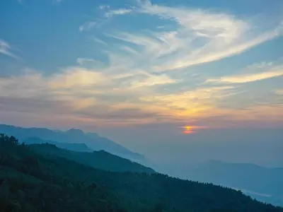 a view of a mountain with the sunset in the sky at DEVASHOLA HOMESTAY in Coonoor