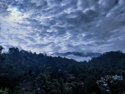 a cloudy sky above a mountain with trees and houses at Raymond's Holiday Homes in Vythiri