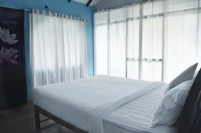 a bedroom with a bed with white sheets and windows at Raymond's Holiday Homes in Vythiri