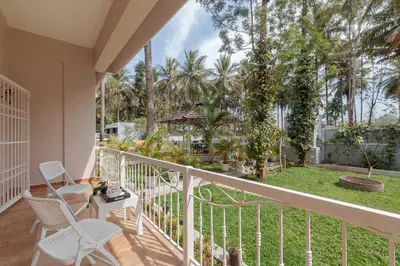 a balcony with chairs and a yard with palm trees at Bask In The Greens Coorg with Private Pool - Pet Friendly - Complimentary Breakfast in Madikeri