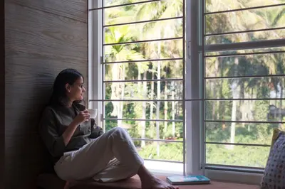 a woman sitting on a window sill looking out at Bask In The Greens Coorg with Private Pool - Pet Friendly - Complimentary Breakfast in Madikeri