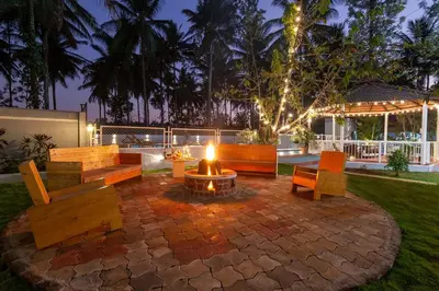 a patio with benches and a fire pit at night at Bask In The Greens Coorg with Private Pool - Pet Friendly - Complimentary Breakfast in Madikeri