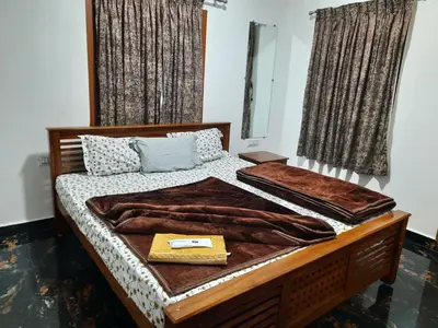 a bedroom with a bed with brown blankets and windows at Kodai Diva Inn - Home Stay in Kodaikānāl