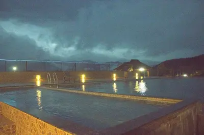 a swimming pool at night with lights in the water at Misty Valley Resort in Varagampadi