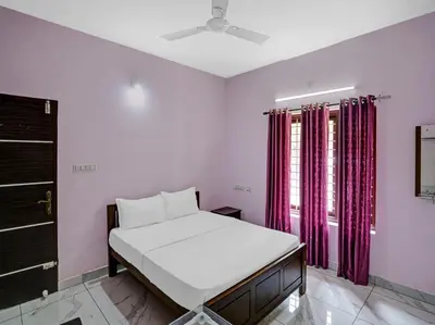 a bedroom with a bed and a window with red curtains at Shalom Palace Residency in Neriyamangalam