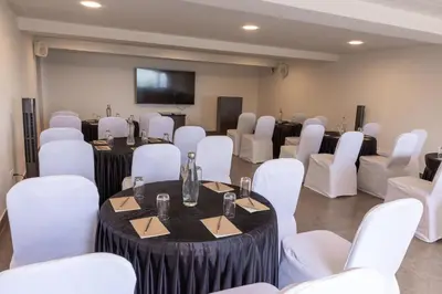a room with white chairs and tables and a flat screen tv at Dvara Luxury Resort Kodaikanal in Kodaikānāl