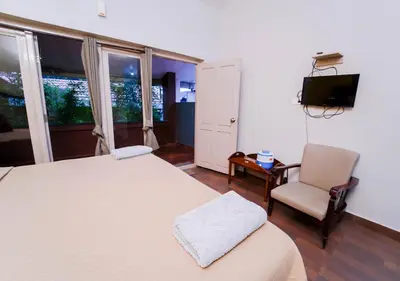 a bedroom with a bed and a chair and a television at SILENT VALLEY FARMSTEAD OOTY by VOYE HOMES in Ooty