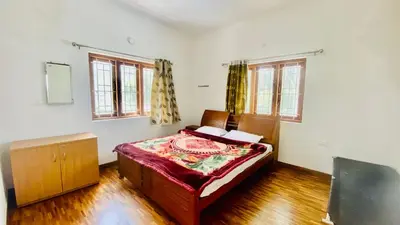 a bedroom with a bed and two windows at Mountain Mansion Kodai in Kodaikānāl