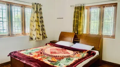 a bedroom with a bed with two chairs and windows at Mountain Mansion Kodai in Kodaikānāl