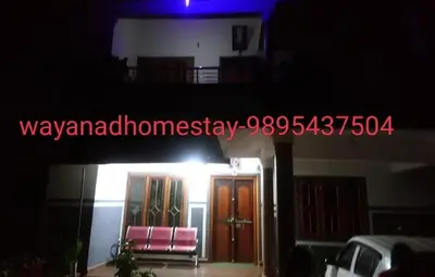 a night view of a house with a door and two chairs at GOLDEN HILL HOMESTAY WAYANAD in Panamaram