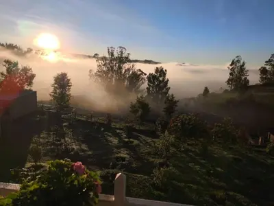 a misty sunrise with the sun rising over a field at Orchard Valley View in Ooty