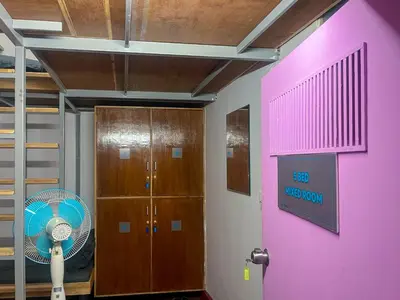 a room with a fan and a pink wall at Rahees Bi Roambay - Backpacker Hostel in Mysore