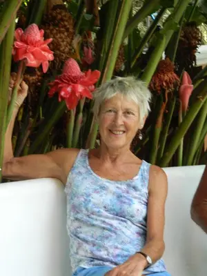 an older woman sitting on a couch in front of a plant at Torch Ginger Homestay in Sultan Bathery
