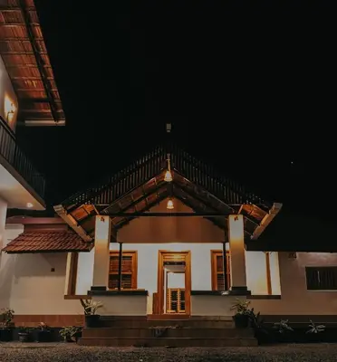 a white house with brown doors at night at PARTHO home stay in Padinjarathara