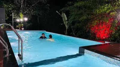 two people in a swimming pool at night at Golden Cypress Resort with Pool -Wayanad in Padinjarathara