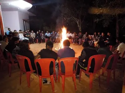 a group of people sitting in chairs in front of a fire at Green Land Estate Homestay 5 Rooms With Garden View in Madikeri