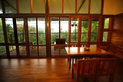 a room with a wooden table and a large window at Solitude Munnar - Tree house in Munnar