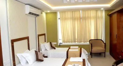 a hotel room with two beds and a chair at Rotano Glitz Inn - Glitz Inn Calicut in Kozhikode