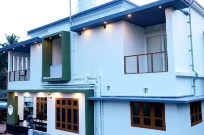 a white house with green doors and windows at Oxygen Home Stay in Agali