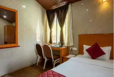 a bedroom with a bed and a desk and a window at Blossom Inn in Coonoor